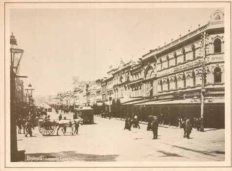 A bustling street scene with horse-drawn carts and early trams, lined with ornate, multi-story Victorian-era buildings, some with signs indicating businesses like "BEATH, SHIRT & CLOTHING CO."