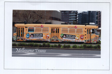 Yellow tram with "M&M's" advertisement featuring characters and the text "DO NOT LICK ADVERTISEMENT" on a city street.