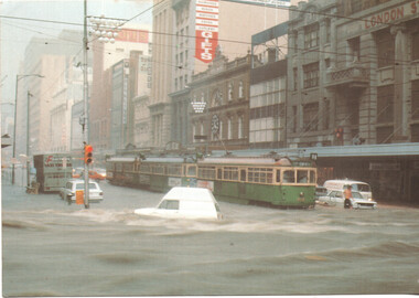Flooded city street with trams and submerged vehicles with traffic lights and buildings.