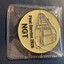 Gold coin with etched image of a modern tram and text reading "First Service 2026 NGT" in a clear plastic sleeve.