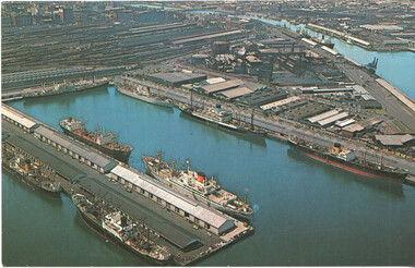 Aerial view of a busy harbor - Melbourne - filled with cargo ships docked along multiple piers and industrial buildings.