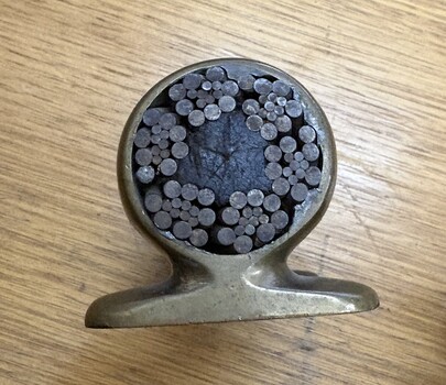 Cross-section of a metal object revealing a dense arrangement of circular metallic rods of varying sizes packed around a central dark core.