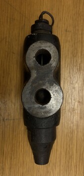 Black cast metal valve body with two ports on the left and a threaded nozzle on the right, shown above a disassembled plunger with a spring clip, threaded housing, and a long metal rod.