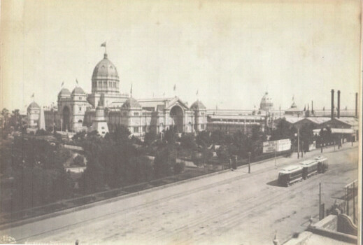 Shows an ornate building with domes and towers. In the background, a cable tram travels along a track past trees and smaller structures.