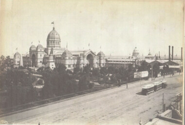Shows an ornate building with domes and towers. In the background, a cable tram travels along a track past trees and smaller structures.