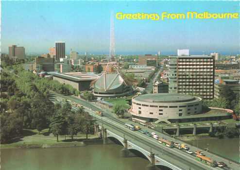 Aerial view of Melbourne cityscape with a prominent spire, a domed building, and a bridge spanning a river, with a line of trams on the bridge and "Greetings From Melbourne" text at the top.