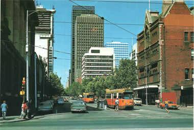 A city street scene with vintage trams and cars, tall buildings, and mature trees under a bright blue sky.