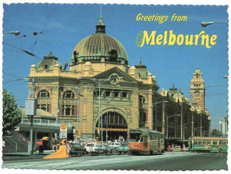 A postcard view of Flinders Street Station in Melbourne, Australia, with a tram in the foreground and cars on the street.