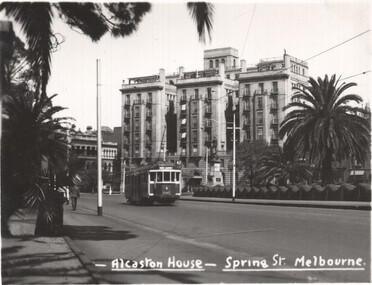 A vintage tram on a street in front of Alcaston House on Spring Street, Melbourne, with palm trees in the foreground.