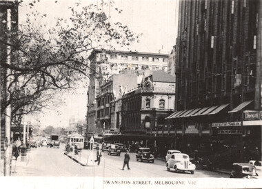 Street scene of Swanston Street in Melbourne, Victoria, showing vintage cars, a tram, pedestrians, and multi-story buildings with awnings.