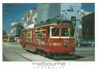 A red and green vintage tram with "City Circle" written on its side, travels on tram tracks in an urban setting with modern buildings in the background under a bright blue sky.