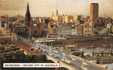 Aerial view of a bustling city skyline, featuring distinctive Gothic revival architecture of a prominent church, modern high-rise buildings, and a busy bridge with traffic.
