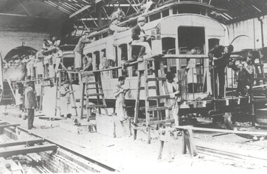 Workers assembling a tramcar in a workshop, with scaffolding and tools visible.
