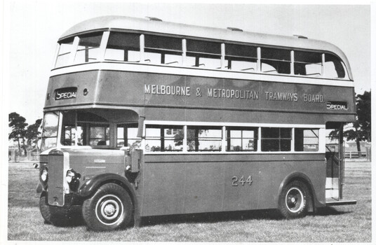 Vintage double-decker bus with "Melbourne & Metropolitan Tramways Board" text and the number 244 on its side, parked on a grassy field.