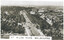 Aerial view of a wide, tree-lined boulevard with heavy traffic, leading towards a cityscape of buildings under a hazy sky, with the text "ST. KILDA ROAD. MELBOURNE" in the foreground.