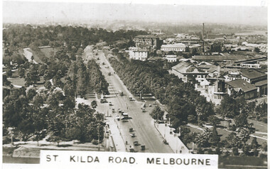 Aerial view of a wide, tree-lined boulevard with heavy traffic, leading towards a cityscape of buildings under a hazy sky, with the text "ST. KILDA ROAD. MELBOURNE" in the foreground.