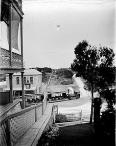 Small steam locomotive drawn tram on a dirt road in a historic town, viewed from a hotel porch.
