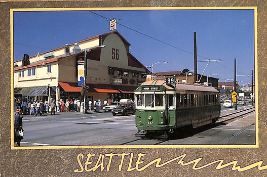 Green vintage streetcar with number 99 on tracks in front of a building with "66" visible, on a sunny day in Seattle.
