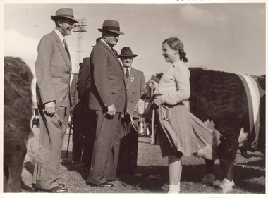 Black and white photograph of cattle judges speaking to a young girl leading a hereford bull