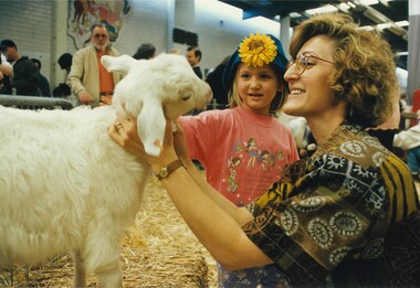 A woman and child petting a white goat in the animal nursery