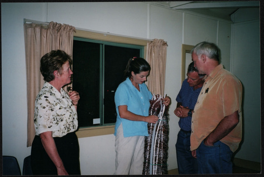 A woman stands holding a large roll of wires and white poles, she is showing two men and one other woman something about this object, they pay close attention.