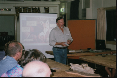 Man stands giving presentation in front of projected image of a fox. The backs of the heads of four people in the audience are visible.