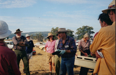 Colour photograph of eight members of Wooragee Landcare Group and local community watching Camille Veselsky demonstrate how to lay a fox bait trap. 