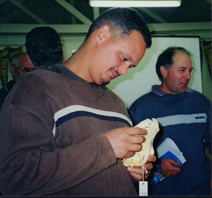 Colour photograph of Simon Feillafe, Kiewa Landcare Coordinator in 2004, examining a quoll skull, with other event attendees in the background. 