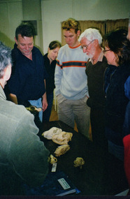 A small group of people gathered around a table observing a selection of fox and quoll skulls. 