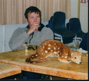 Taxidermied spotted-tailed quoll on a table with an unknown man sitting behind it. 