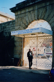 Man standing in front of a white gate with a sign saying "H.M Integration Prison Beechworth"
