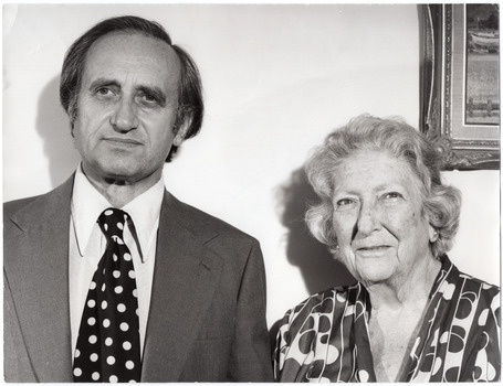 B&W portrait of two people standing side by side. The man is wearing a suit and shirt, and a dark tie with polka dots. The woman is wearing a dress or shirt with a bold geometric pattern.