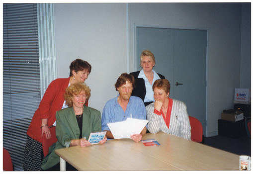 COL photo of five people gathered around the end of a table, looking at some publications on the table in front of them.