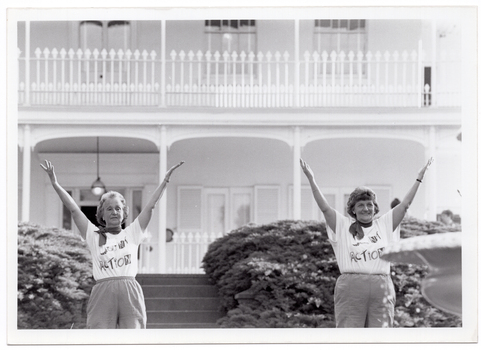B&W photo of two women conducting an exercise demonstration. They are in the garden of a large two-storey house, which is in the background.