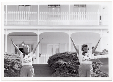 B&W photo of two women conducting an exercise demonstration. They are in the garden of a large two-storey house, which is in the background.