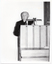 B&W photo of a man standing at a podium built into a large wooden desk.