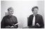 B&W photo of two women standing behind a podium (partially obscured). One of the women is holding an award trophy.