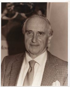 B&W portrait of a man wearing a suit and tie. He has a slight smile on his face.