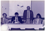 B&W photo of a man standing behind a long rectangular table at which three others are seated. He is looking straight ahead and speaking. Two of the three seated people are looking down at some paperwork, while the other is looking to one side, beyond the camera. The people seated are all smiling, to varying degrees. On the wall behind them is a large Arthritis Foundation of Victoria banner.