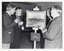 B&W photo of four men gathered around a painting sitting on an easel. One of the men is holding a beer glass, while the other three men are each holding a glass of champagne. Affixed to the easel (below the painting) is a sign with the text, "WINNER Open Competition".
