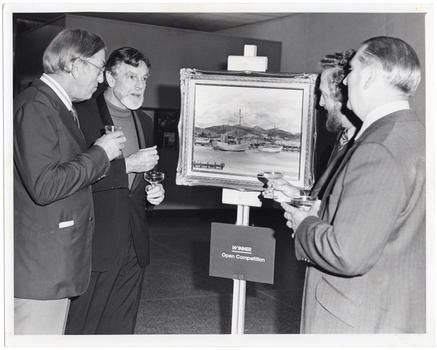 B&W photo of four men gathered around a painting sitting on an easel. One of the men is holding a beer glass, while the other three men are each holding a glass of champagne. Affixed to the easel (below the painting) is a sign with the text, "WINNER Open Competition".