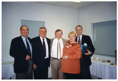 COL photo of a group of five people (standing), posing for a photo. Behind them are some tables covered in white tablecloths, with cups and saucers, bowls, and an urn.