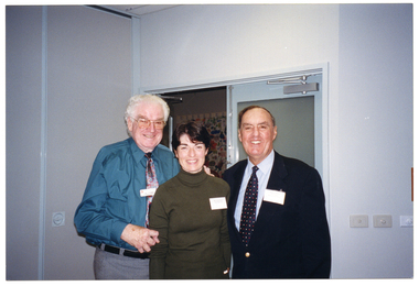 COL photo of three people posing for a photo in front of an open doorway. There is a colourful floral curtain or blind covering the window in the adjoining room.