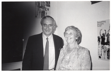B&W photo of two people standing in the corner of a room, smiling. Behind them is a poster on each wall, depicting people exercising. The poster on the right includes the text "Life Be In It" and "Something for every body!"