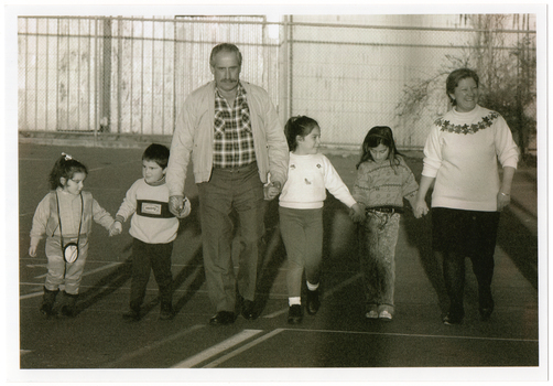 B&W photo of two adults and four children walking hand in hand on an outdoor sports court.