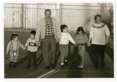 B&W photo of two adults and four children walking hand in hand on an outdoor sports court.