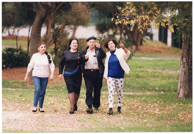 COL photo of a small group of people walking in a park. Some of them are pointing up as they all look towards something outside of the frame.