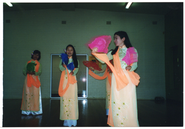 COL photo of four dancers (one partially obscured), wearing traditional Vietnamese dress. They are performing a dance with colourful hand-held fans.