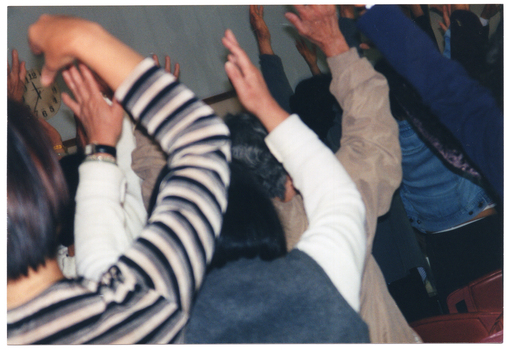 COL close up photo of seminar participants from behind, as they raise their arms up above their shoulders.