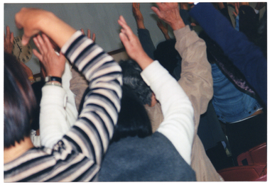 COL close up photo of seminar participants from behind, as they raise their arms up above their shoulders.